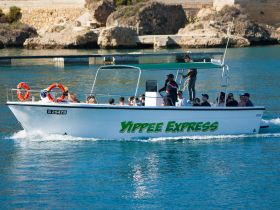 The 'Yippee Express' boat is seen cruising through clear waters with a lively group of passengers enjoying their time on board, perfect for adventure seekers.