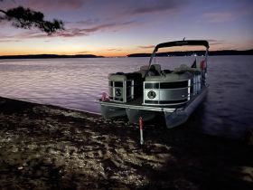 A serene view of a pontoon boat docked at the water's edge during sunset, creating a picturesque scene perfect for evening outings.