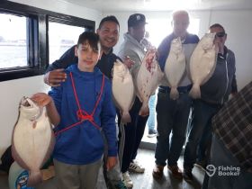 A group of anglers proudly displays their catch of flounder aboard a fishing boat, celebrating a successful day on the water.