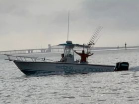 A fishing boat named 'Second Chance' is seen on the water with two people aboard, one celebrating with arms raised — a perfect moment capturing the joy of a day on the water.