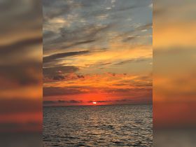 A stunning sunset over the ocean, casting vibrant colors across the sky and water, perfect for a serene evening on the boat.