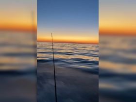 A serene sunset view over the ocean with a fishing rod in the foreground, capturing the tranquil essence of a fishing trip at dusk.