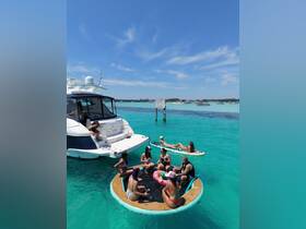 A lively group enjoys a fun day on the water, relaxing on a floating mat and sipping cocktails near a luxurious yacht in the beautiful turquoise waters.