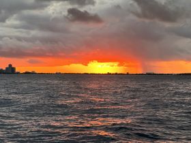 A stunning sunset casts vibrant colors over the water, with a picturesque skyline in the background — a perfect moment for evening boat cruises.