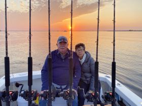 A couple enjoys a serene fishing trip at sunset, surrounded by fishing rods on their boat — a perfect moment for relaxation and adventure on the water.