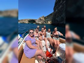 A lively group of friends enjoys a sunny day on a boat, celebrating together against a stunning coastal backdrop — perfect for summer adventures and memorable outings.