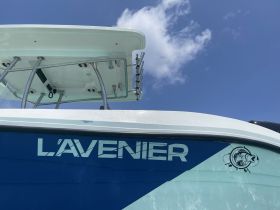 A close-up view of the side of the boat named 'L'Avenier', showcasing its sleek design against a clear blue sky.
