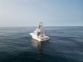 A fishing boat named 'Knot Tuggin' is seen on calm ocean waters with people onboard, showcasing a perfect day for fishing adventures.
