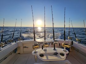 A serene view from the back of a fishing boat, showcasing fishing rods and reels against a stunning sunset backdrop — perfect for deep-sea fishing enthusiasts.