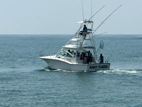 A fishing boat named 'Knot Tuggin' navigates the waters with a group of anglers on board, showcasing the excitement of a day on the water.
