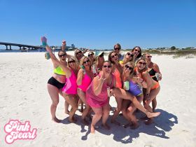 A lively group of friends celebrates on the beach, enjoying drinks and fun in the sun — perfect for bachelorette parties or summer getaways.