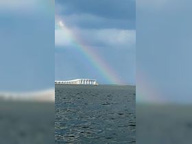 A stunning view of a rainbow arching over a bridge, set against a tranquil water backdrop — a picturesque moment capturing nature's beauty.
