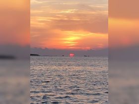 A stunning sunset over the water, with silhouettes of boats in the distance, creating a picturesque scene perfect for evening cruises.