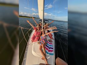A joyful group of friends celebrates aboard a sailboat, enjoying the sun and water during a perfect sunset cruise.