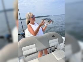 A woman proudly displays her catch while fishing on a boat, showcasing the joy of a successful day on the water.