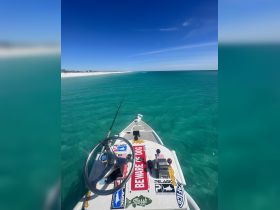 A close-up view of the helm and console of a fishing boat, showcasing the steering wheel and fishing rod, set against a backdrop of stunning turquoise waters.