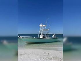 A sleek speedboat is docked on a sandy beach, showcasing its fishing gear and inviting waters — perfect for a day of adventure on the ocean.