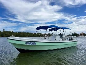 A sleek boat named 'Wet Tuna' glides through calm waters, showcasing its stylish design and blue canopy against a picturesque backdrop.