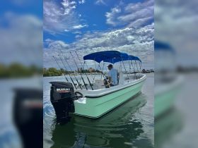 A fishing boat with a sleek design is anchored, showcasing its fishing rods and Suzuki motor, perfect for a day on the water.