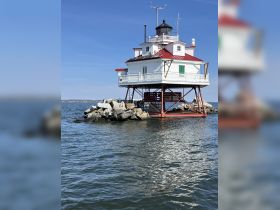 A scenic view of a lighthouse standing on stilts over the water, surrounded by rocks. This iconic structure adds charm to the coastal landscape.