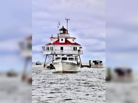 The 'Bay Hunter II' approaches a picturesque lighthouse on the water, showcasing a scenic maritime experience with boats in the background.