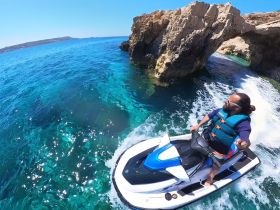 A thrilling moment captured on a jet ski, navigating through crystal-clear waters near stunning rock formations — perfect for adventure seekers exploring the coastline.