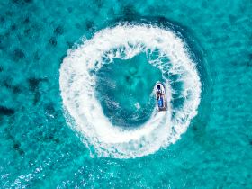 An exhilarating aerial view of a jet ski making waves in crystal-clear turquoise waters — perfect for adventure seekers enjoying water sports.