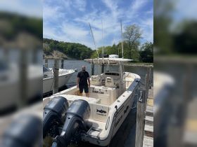 A man stands on the dock beside a sleek fishing boat equipped with twin Yamaha engines, showcasing the perfect vessel for fishing adventures in Muskegon, MI.