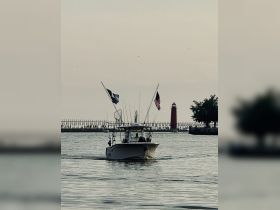 A fishing boat navigates the waters near a lighthouse, showcasing a serene evening on the water — perfect for fishing enthusiasts and sunset cruises.