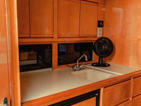 Interior view of a boat's kitchen area featuring a microwave, sink, and fan, showcasing the cozy amenities available for onboard dining and comfort.