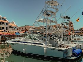 A sleek yacht docked at the marina, showcasing its impressive structure against a vibrant backdrop of shops and restaurants.