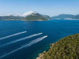 A stunning aerial view of multiple boats cruising through crystal-clear waters, surrounded by lush green hills and a picturesque coastline — perfect for showcasing the beauty of the region.