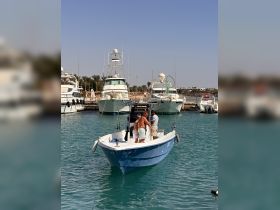 A group of friends prepares for a fishing adventure aboard a small boat in a bustling harbor, surrounded by larger yachts — perfect for a day of fun on the water.