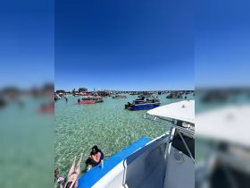 Guests enjoy a vibrant sandbar stop, relaxing in the clear waters while surrounded by various boats — a perfect day for fun and sun on the water.