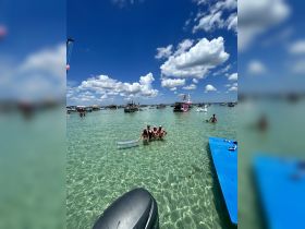 A group of friends enjoys a fun day at the sandbar, swimming in crystal-clear waters surrounded by boats — a perfect summer getaway.