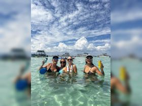 A fun group of friends enjoys a lively sandbar stop, celebrating with drinks in the shallow, clear waters — perfect for summer adventures on the water.