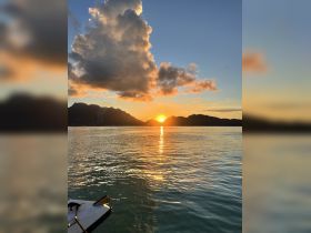 A stunning sunset over tranquil waters, with mountains in the background and a boat's edge visible in the foreground — perfect for capturing the beauty of evening cruises.