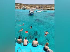 A lively scene of guests enjoying a sunny day in crystal-clear turquoise waters, with some swimming and others relaxing on the boat's edge — perfect for summer adventures.