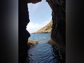 A stunning view from inside a cave looking out towards the coastline, showcasing the beautiful interplay of rock formations and tranquil waters.