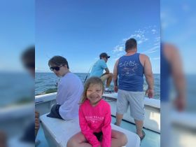 A joyful child smiles while sitting on a fishing boat, surrounded by family members enjoying a day on the ocean — perfect for creating lasting memories on the water.