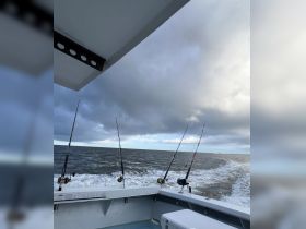 A scenic view from the deck of a fishing boat, showcasing fishing rods against a backdrop of rolling waves and a cloudy sky — perfect for a day of deep-sea fishing adventures.