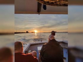 A group of friends enjoys a serene sunset on a fishing boat, capturing the perfect moment of relaxation and camaraderie on the water.