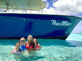 A joyful group of four women, including two minors, enjoys a refreshing swim in crystal-clear waters beside the boat named 'PeaceMaker' — a perfect snapshot of fun and relaxation on the water.