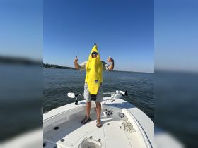 A man dressed in a playful banana costume gives a thumbs up while standing on the deck of a boat, capturing a fun and lighthearted moment on the water.