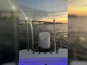 A scenic view from the back of a boat as it navigates through calm waters at sunset, showcasing the engine and fishing rods against a picturesque backdrop.