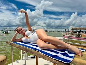 A woman relaxes on a boat deck under a sunny sky, enjoying a vibrant day on the water surrounded by other boats — perfect for summer parties and fun outings.