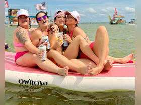 A fun group of friends enjoys a sunny day on a floating mat, sipping drinks and celebrating together in the water — perfect for summer parties and beach outings.
