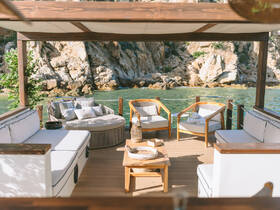 A beautifully designed lounge area on a boat, featuring comfortable seating and a serene view of rocky shores — perfect for relaxation and enjoying the scenery.