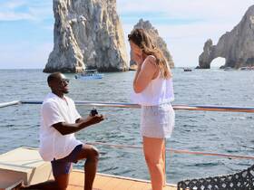 A romantic proposal takes place on a boat in Cabo San Lucas, with stunning rock formations in the background, creating a perfect setting for unforgettable moments.