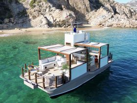 Aerial view of a stylish boat anchored near a sandy beach, showcasing its spacious deck and modern design — perfect for relaxing on the water.